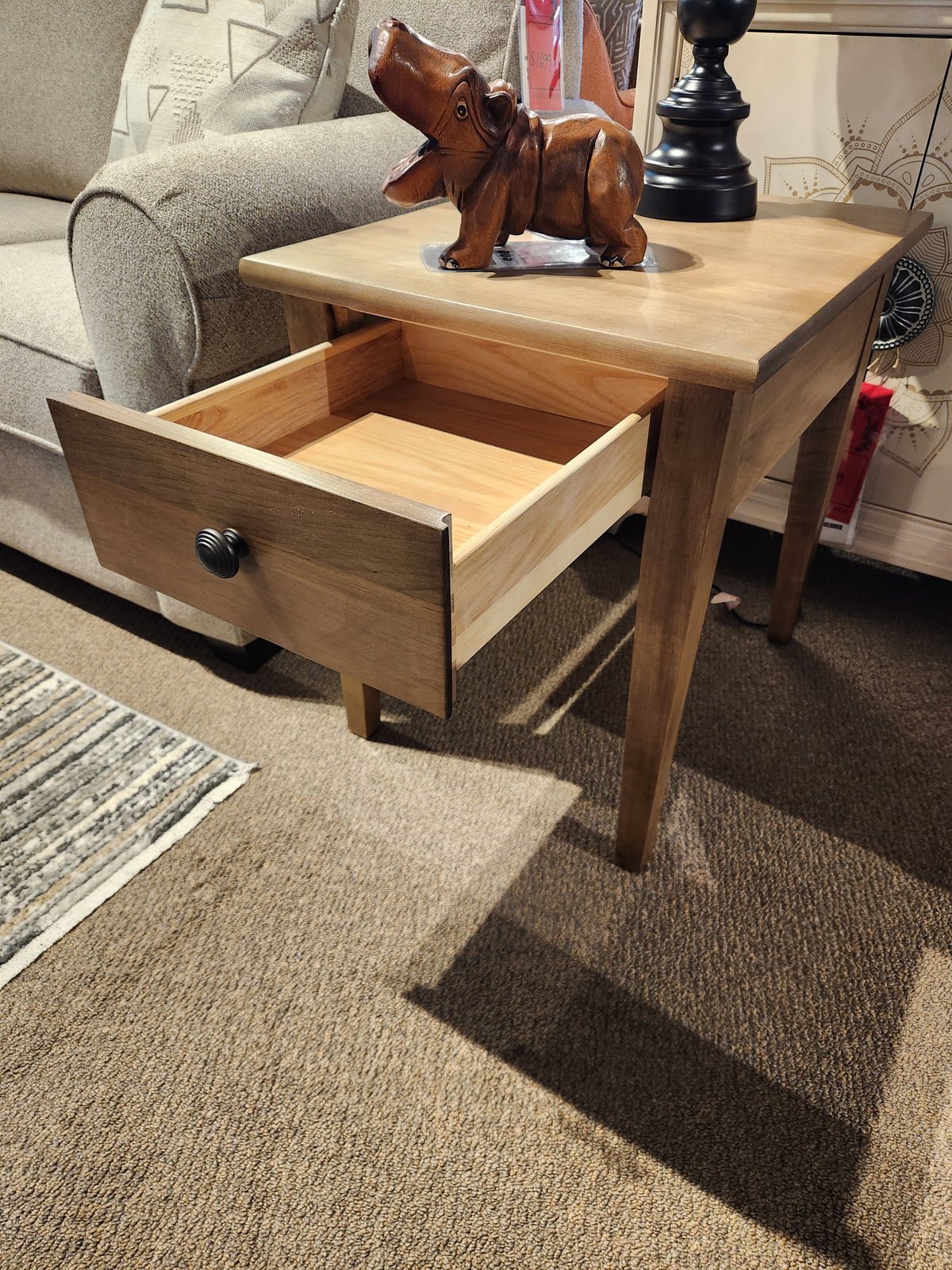 A Durham 905 20"x24" end table with a drawer in Champagne finish sits on a carpeted floor.