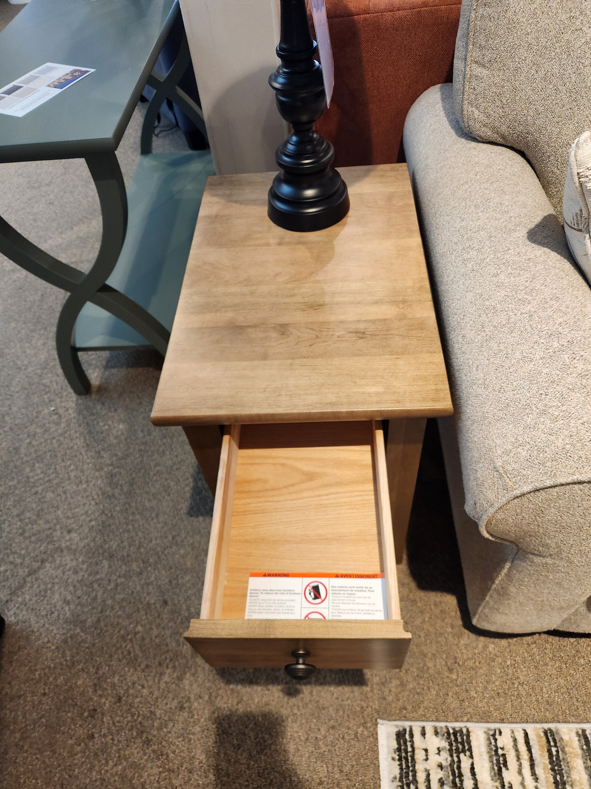 A Durham 905 16" x 24" End Table in Champagne with a drawer sits by a beige sofa, topped with a black lamp.