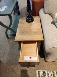 A Durham 905 16" x 24" End Table in Champagne with a drawer sits by a beige sofa, topped with a black lamp.