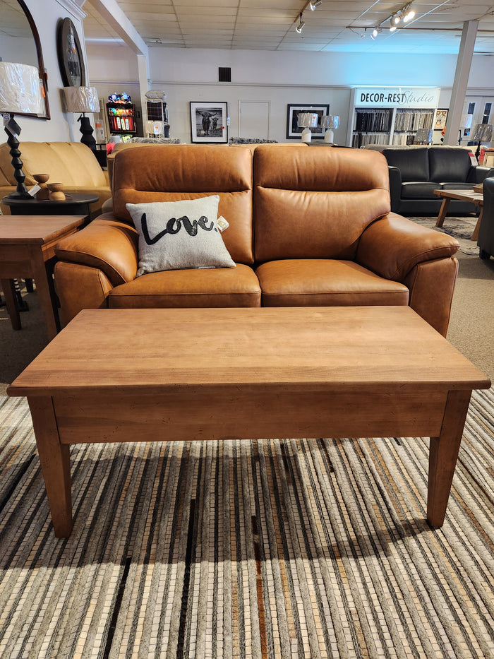 Brown leather loveseat with a "Love" pillow behind Durham's 905 Cocktail Table (48x24", Aged Wheat) on a striped rug.