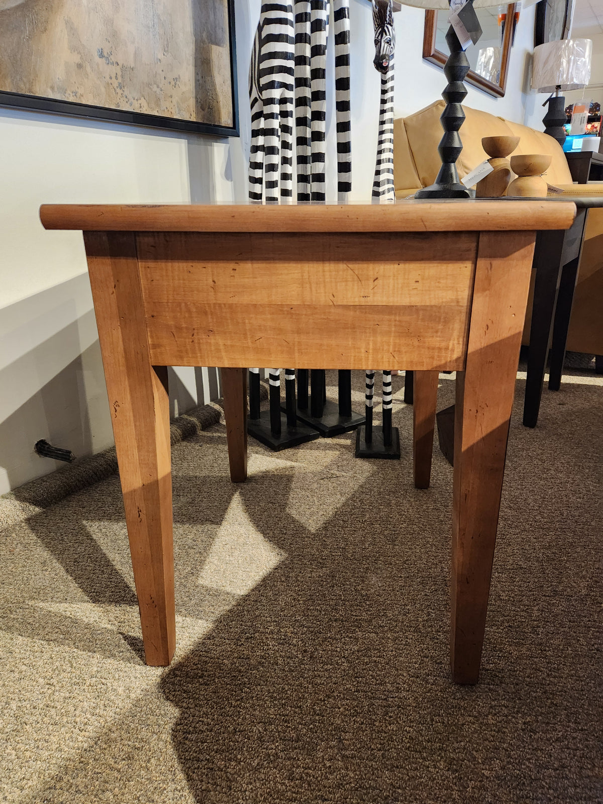 The Durham 905 20" x 24" End Table in Aged Wheat with tapered legs is displayed on a carpeted showroom floor.