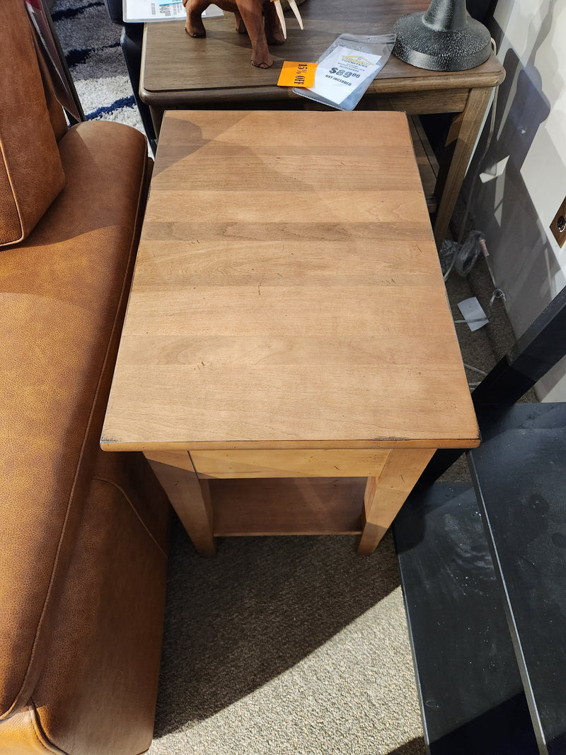 The Durham 905-16" x 24" End Table in Aged Wheat sits by a brown sofa, ideal for modern or transitional décor.