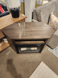 The Durham 905-Open Corner Cabinet With Logs in Firebox sits on carpet near a sofa and lamp, glass doors displayed.