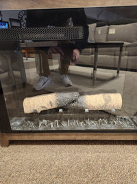 A man is reflected on the glass front of a Durham 905-Open Corner Cabinet with logs in the firebox in a living room.