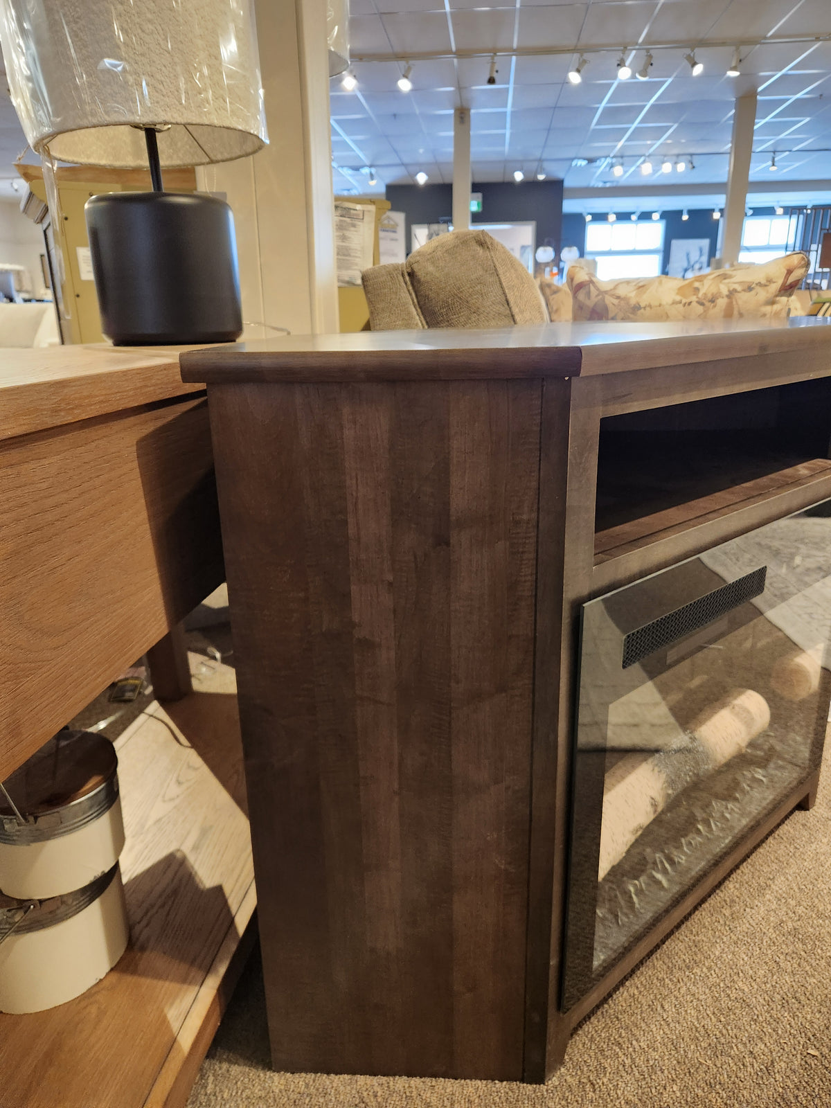 Durham 905-Open Corner Cabinet With Logs in Firebox, displayed beside a light wood table in a showroom.