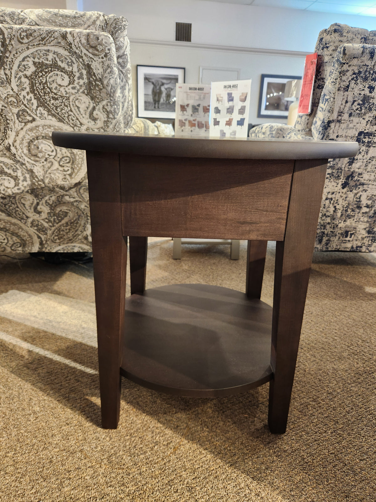 Durham 905- 24" Round Table w/Shelf in Java, shown with patterned chairs in the background.