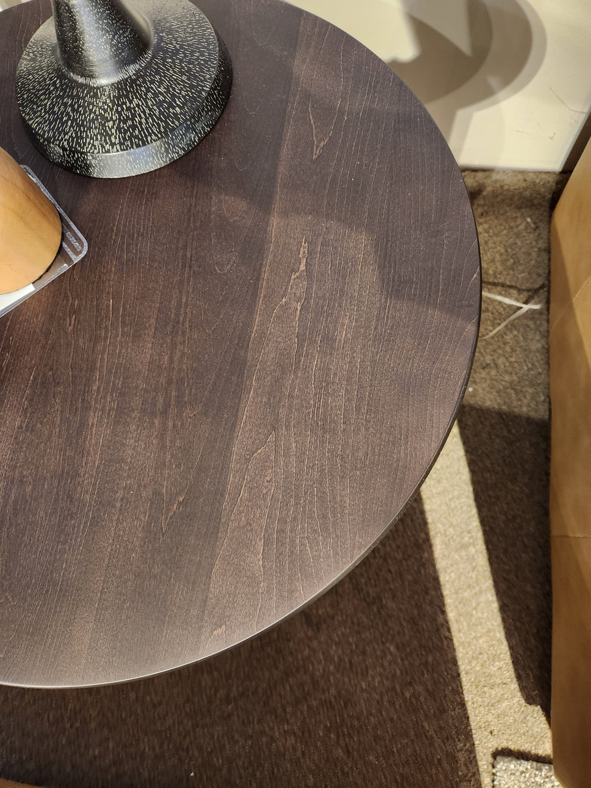 Durham 905- 24" Round Table in Java; sunlight casts shadows across its compact surface on a carpeted floor.