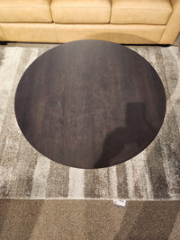 Durham 905-40" Round Cocktail Table in Java sits on a patterned rug in front of a tan leather sofa.