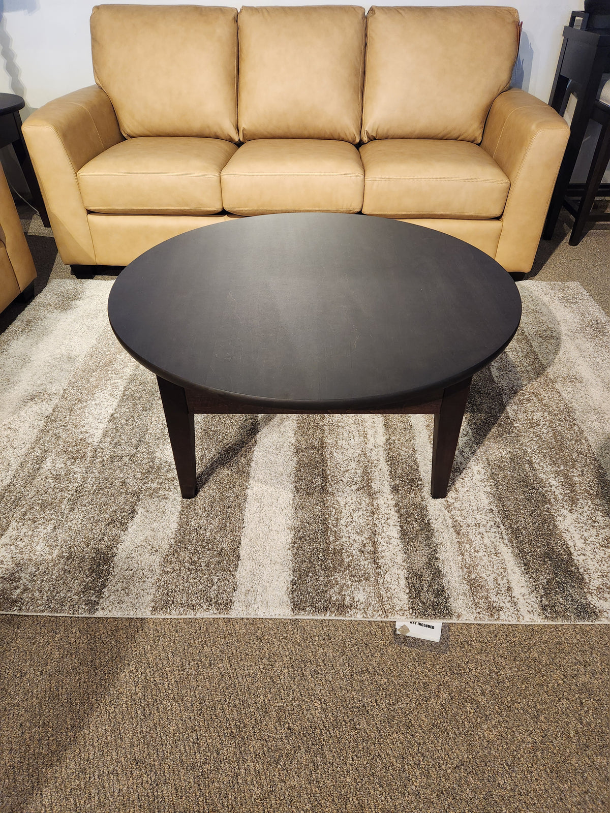 A Durham 905 40" round cocktail table in Java rests on a rug in front of a tan leather sofa.