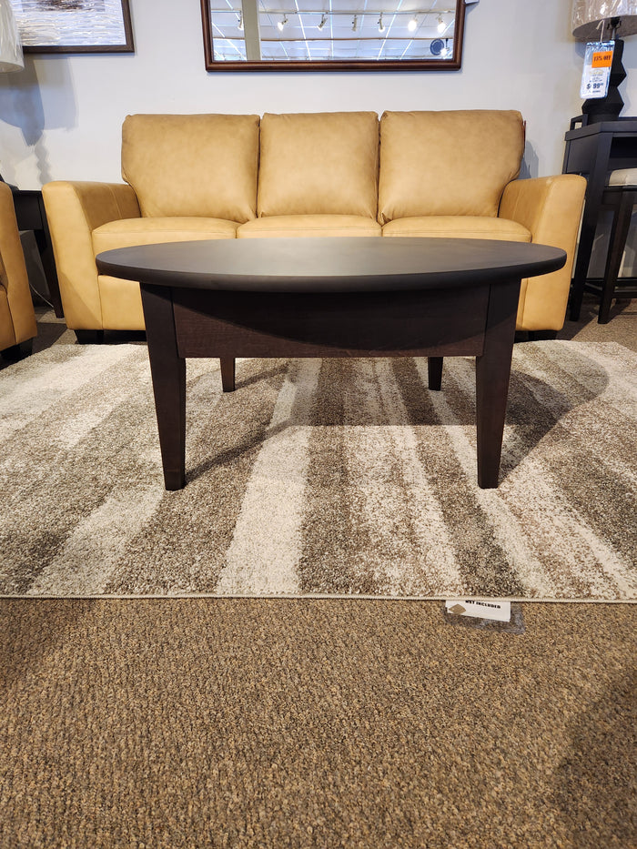 The Durham 905- 40" Round Cocktail Table in Java is displayed on a rug before a tan sofa in the showroom.