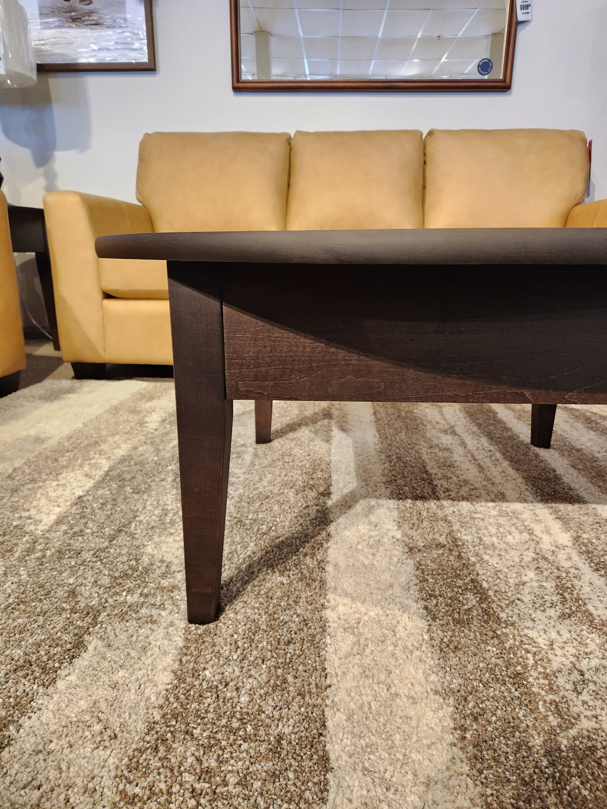 The Durham 905 40" Round Cocktail Table in Java stands out before a tan couch on a beige patterned carpet.