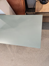 The Durham 900- Transitional Sofa Table in pale green glass stands over a beige carpet by a wooden side table and brown seat.