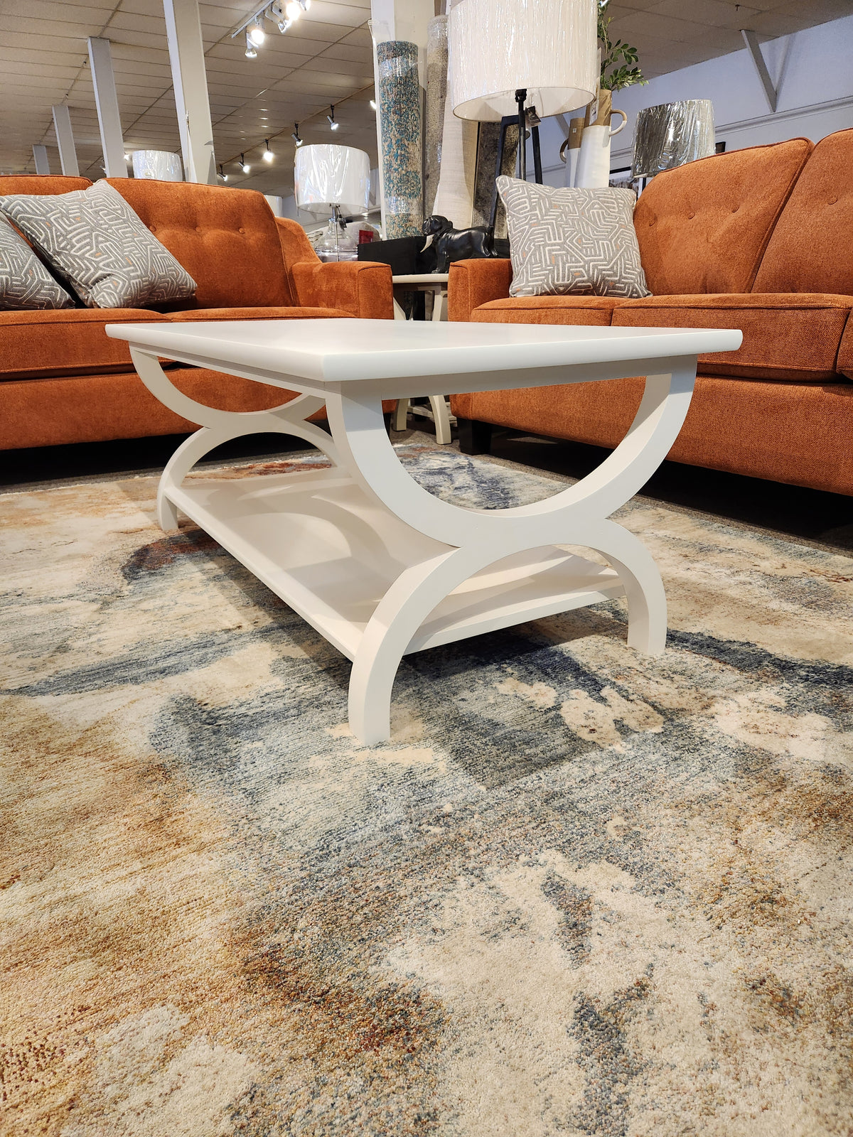 Durham 900-503 Transitional Cocktail Table with curved legs sits on a rug between two orange sofas in the showroom.