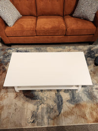 The Durham 900-503 Transitional Cocktail Table is a white rectangular piece placed before an orange sofa on a rug.