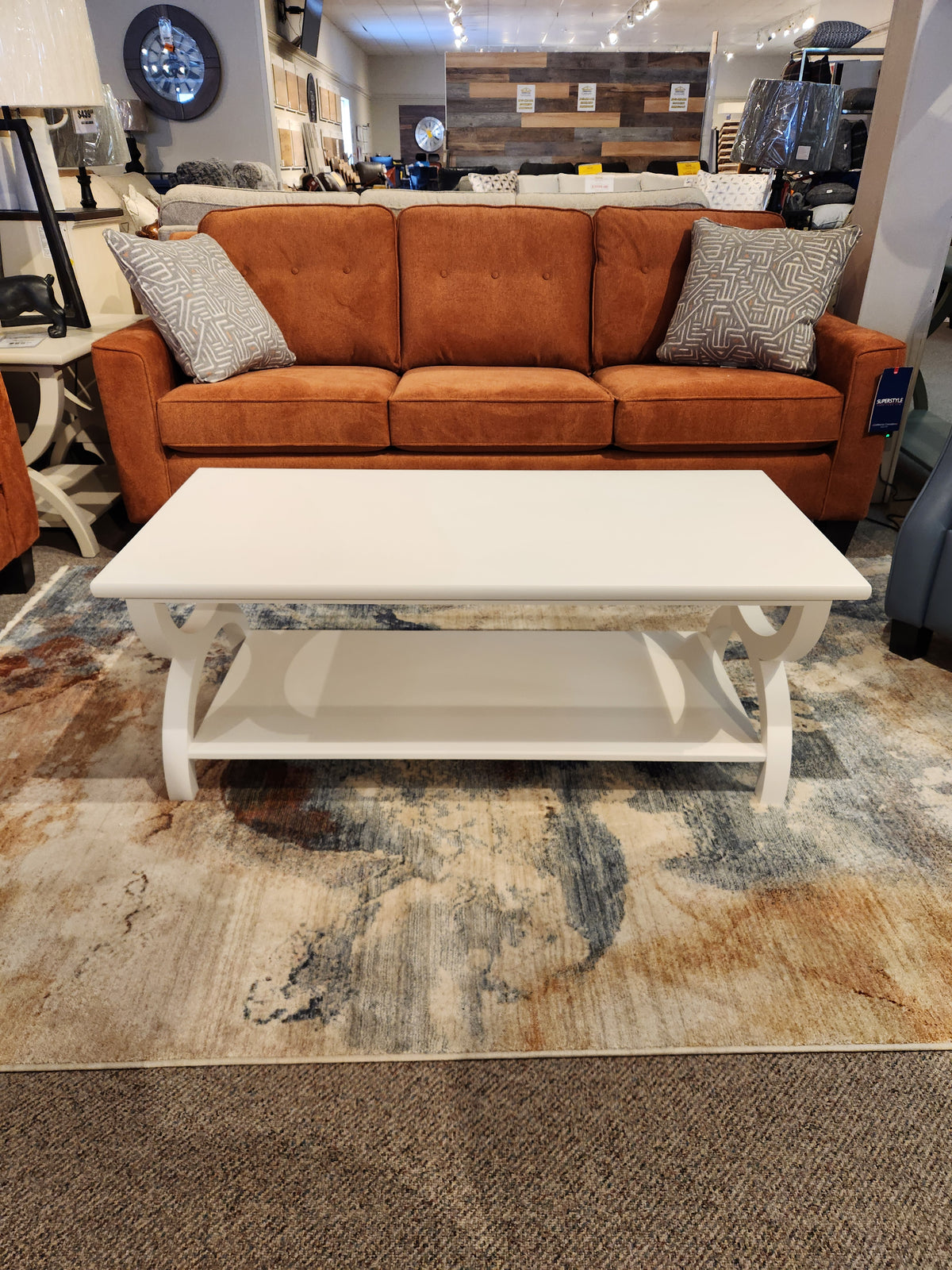 A brown sofa with patterned pillows sits behind Durham’s 900-503 Transitional Cocktail Table on a multicolored rug.