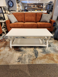 A brown sofa with patterned pillows sits behind Durham’s 900-503 Transitional Cocktail Table on a multicolored rug.