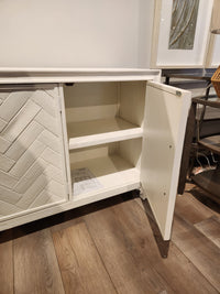 Jofran Gramercy 3 Door Accent Cabinet with chevron inlay, two shelves, and open door on wood floor.