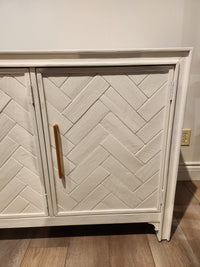 The Jofran Gramercy 3 Door Accent Cabinet features a chevron inlay, gold handles, and sits on a light wood floor.