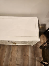 Jofran Gramercy 3 Door Accent Cabinet with wire-brushed finish on light wood floor, power outlet nearby.