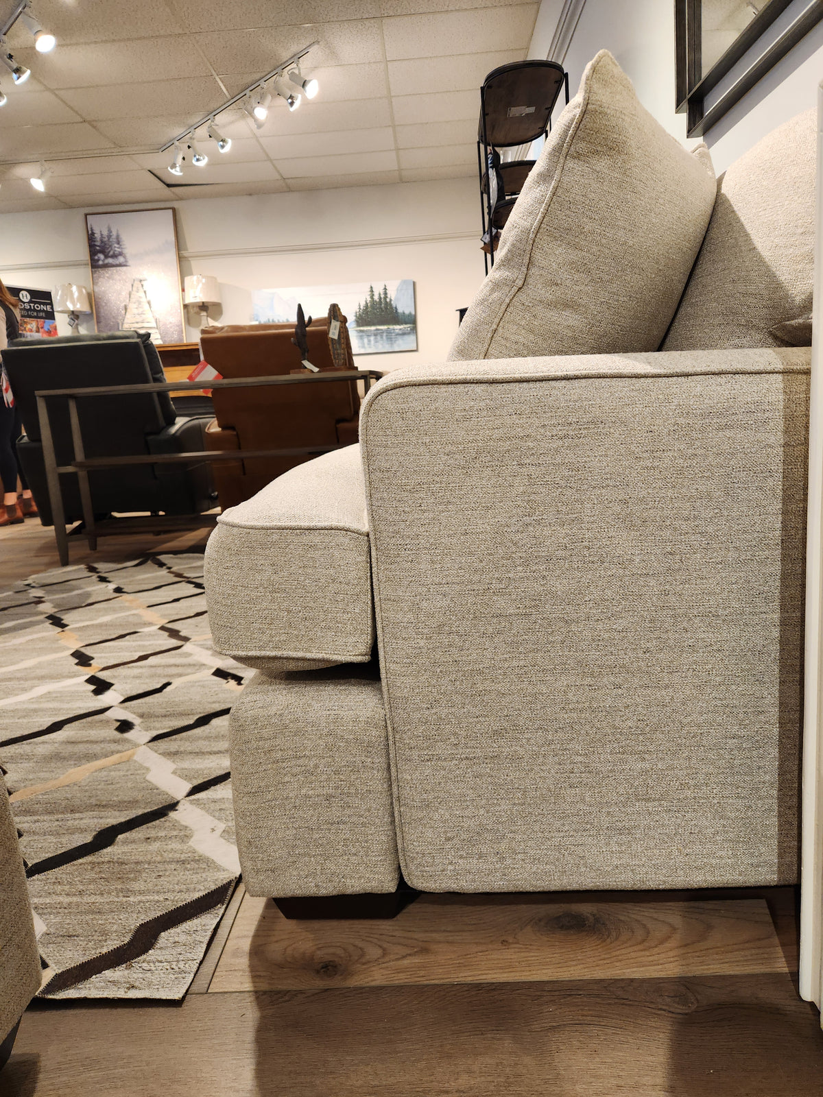 Side view of the beige La-z-boy 663 Paxton Sofa with ComfortCore® cushions in a showroom, other chairs in background.