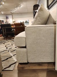 Side view of the beige La-z-boy 663 Paxton Sofa with ComfortCore® cushions in a showroom, other chairs in background.