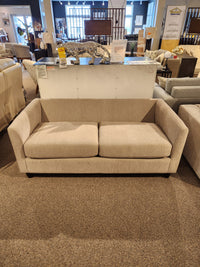 The Best Bayment Double Sofa Bed in beige is showcased in a showroom with other sofas and decor in the background.