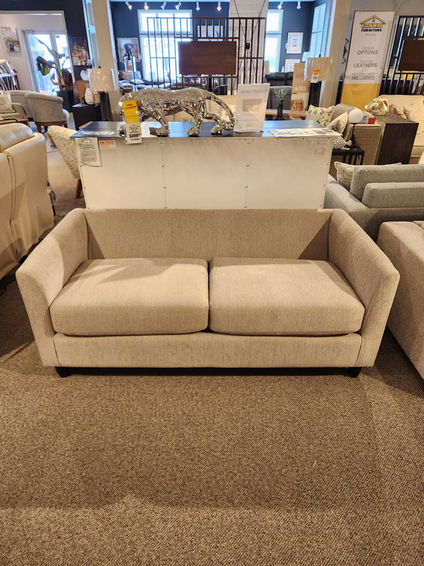 The Best Bayment Double Sofa Bed in beige is showcased in a showroom with other sofas and decor in the background.