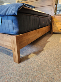 A Vokes 247 Saugeen King Bed Frame with blue mattress is beside a wooden nightstand on a carpeted floor.