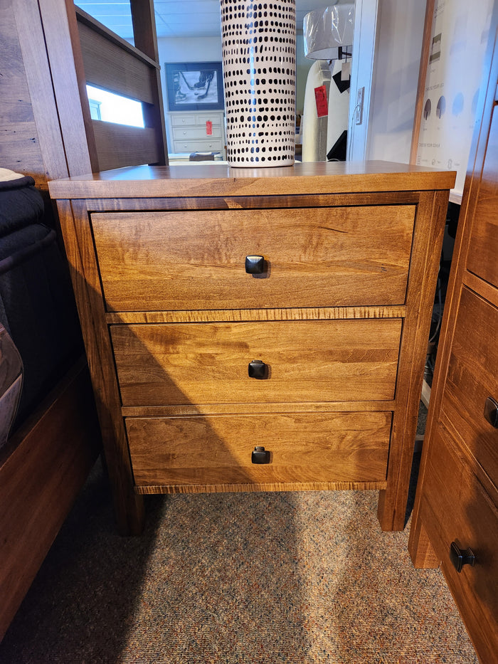 The Vokes 247 Saugeen 3 Drawer Nightstand with black handles sits on carpet beside a bed and other furniture.