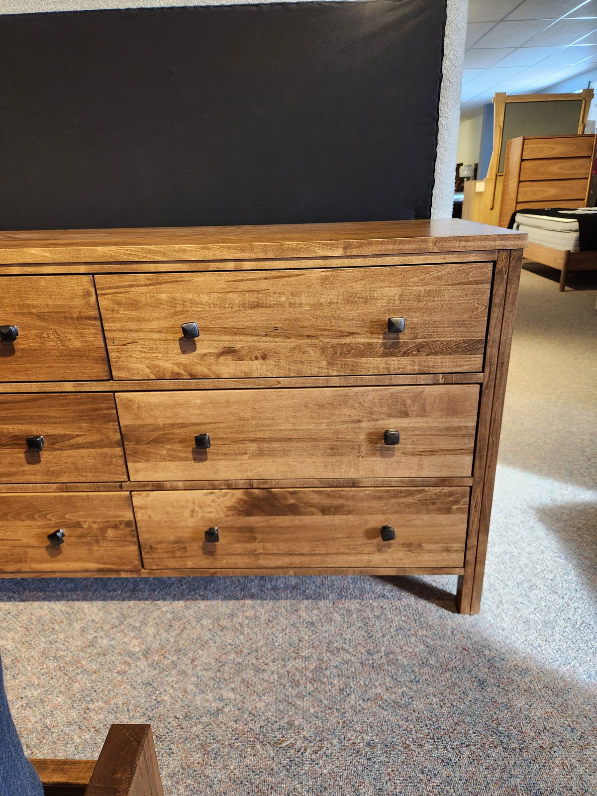 The Vokes 247 Saugeen 6 Drawer Dresser with square black handles is displayed in a furniture showroom.