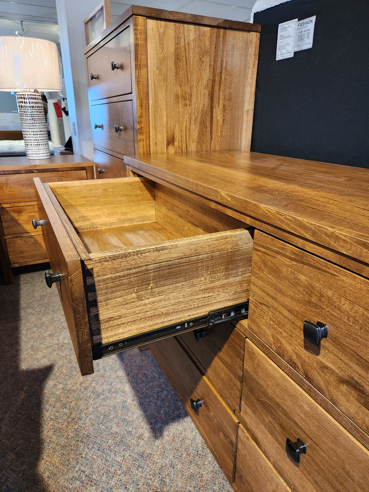 The Vokes 247 Saugeen 6 Drawer Dresser features black knobs and a smooth rustic wormy maple finish in a showroom.