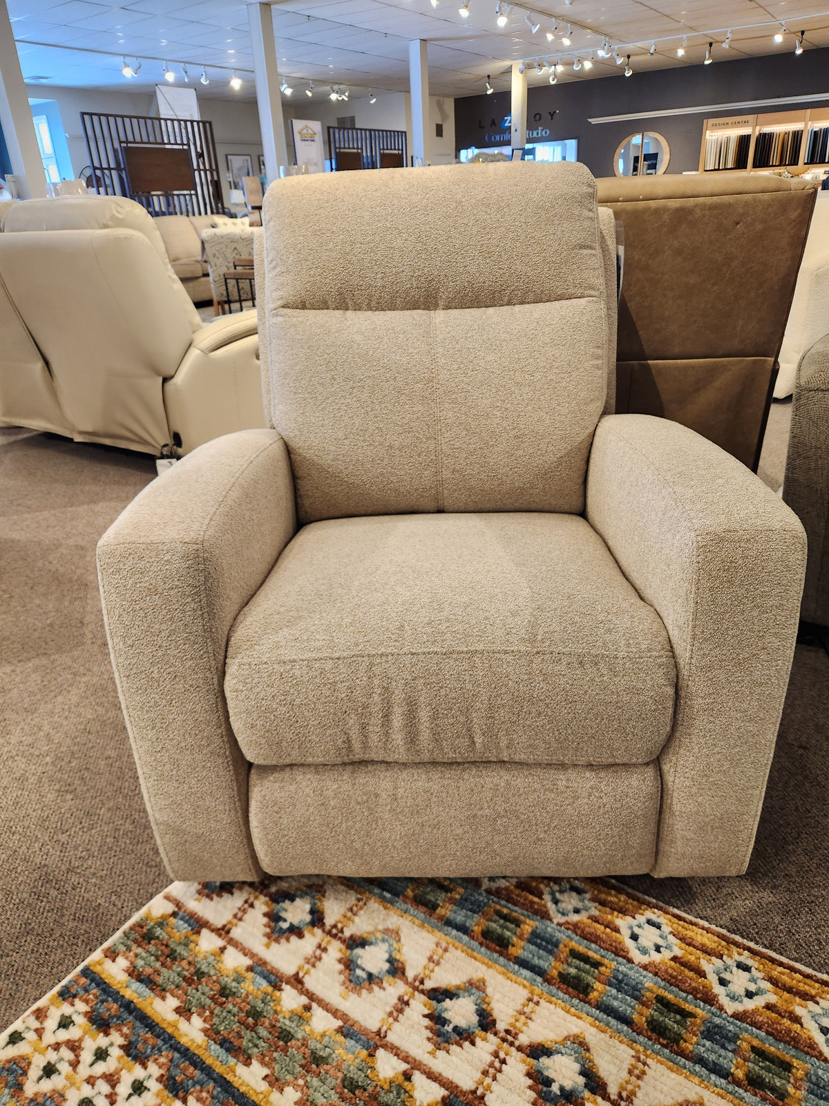 The Aurora Furniture 88365 Muskoka Power Reclining Chair is displayed on a patterned rug in the showroom.