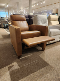 The Palliser 77171 Soren Push-Back Reclining Chair, in brown leather with wooden legs and footrest, shown in a showroom.