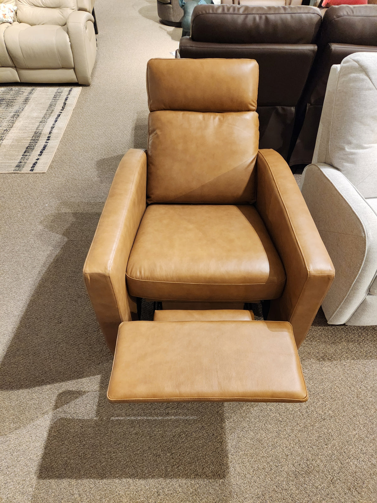 The Palliser 77171 Soren Push-Back Reclining Chair features brown leather and tapered wooden legs, shown in a showroom.