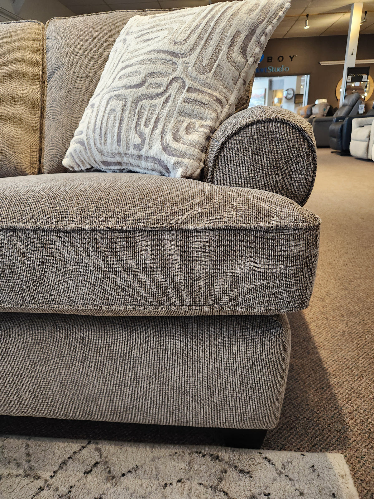 Close-up of the Decor-rest 2285 Sofa with Chaise and a patterned throw pillow in a furniture showroom.