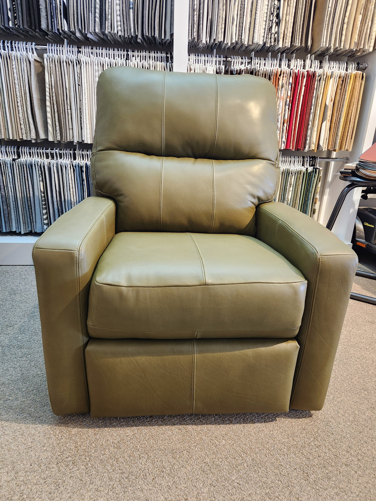 Decor-rest M38505 green leather power reclining chair with headrest shown in showroom, fabric samples in background.