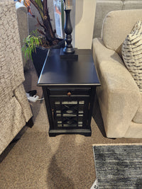 The Jofran 275 Craftsman Power Chairside End Table with antique hardware sits between two beige couches.