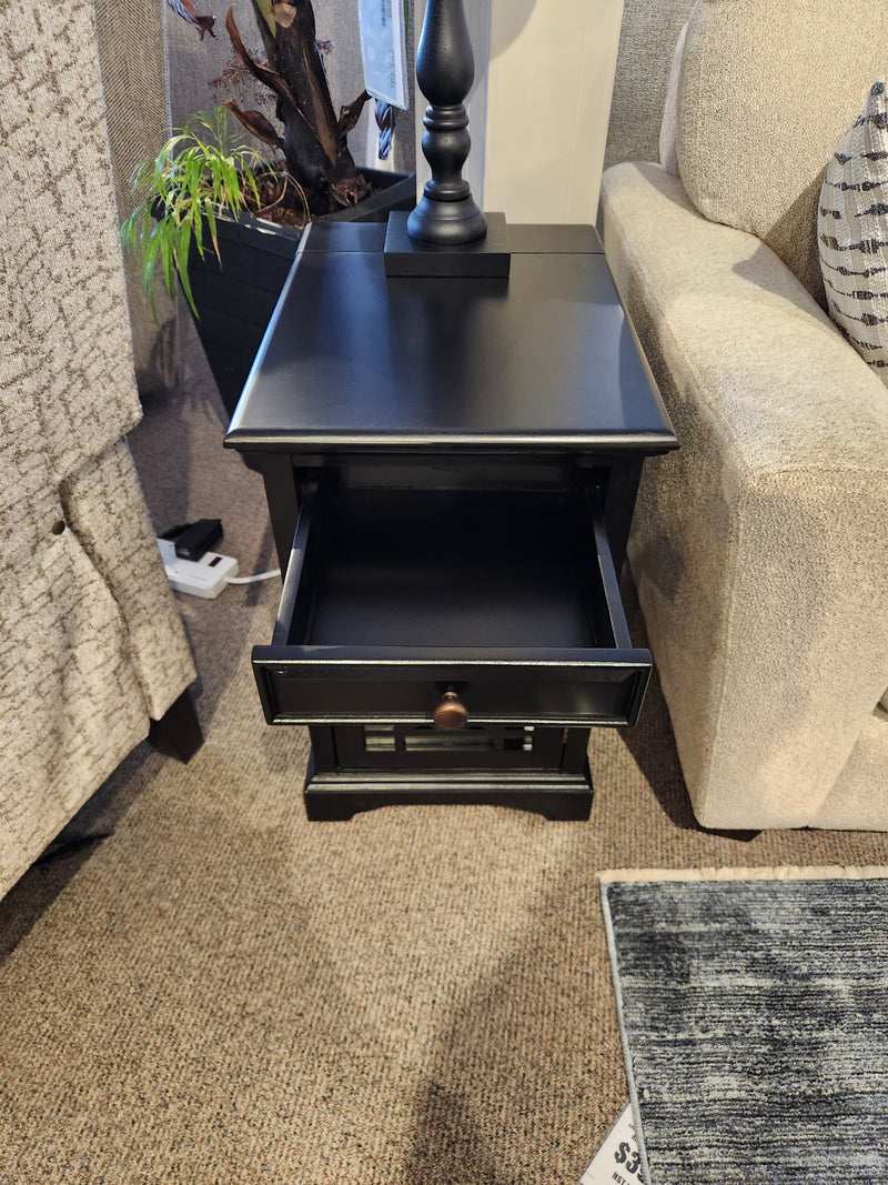 The Jofran 275 Craftsman Power Chairside End Table sits between two sofas on a carpeted floor.
