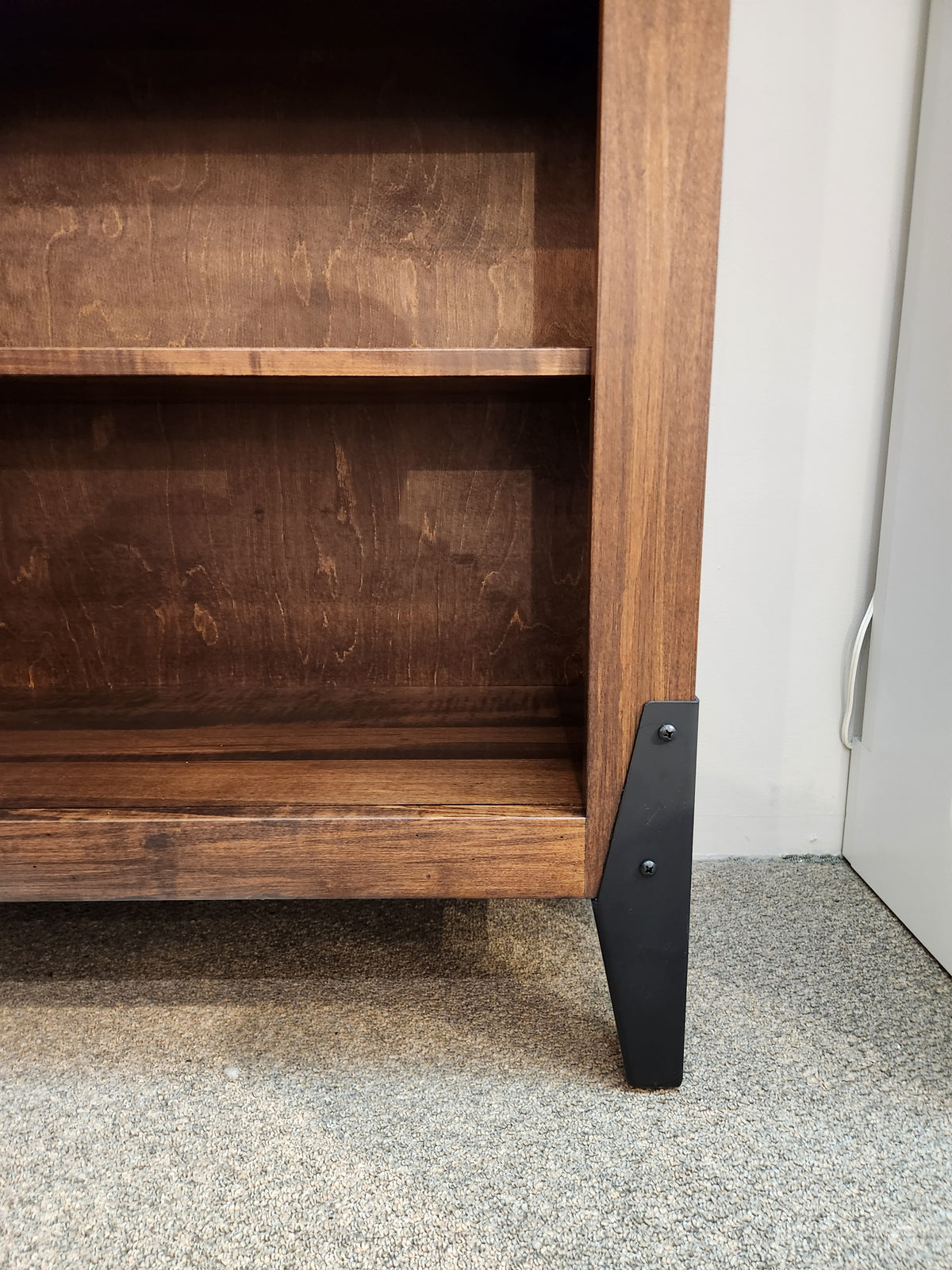 A close-up of a Handstone CH80 Chattanooga 80" Bookcase's black metal leg and maple mocha finish on carpet.