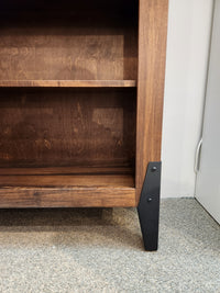 A close-up of a Handstone CH80 Chattanooga 80" Bookcase's black metal leg and maple mocha finish on carpet.