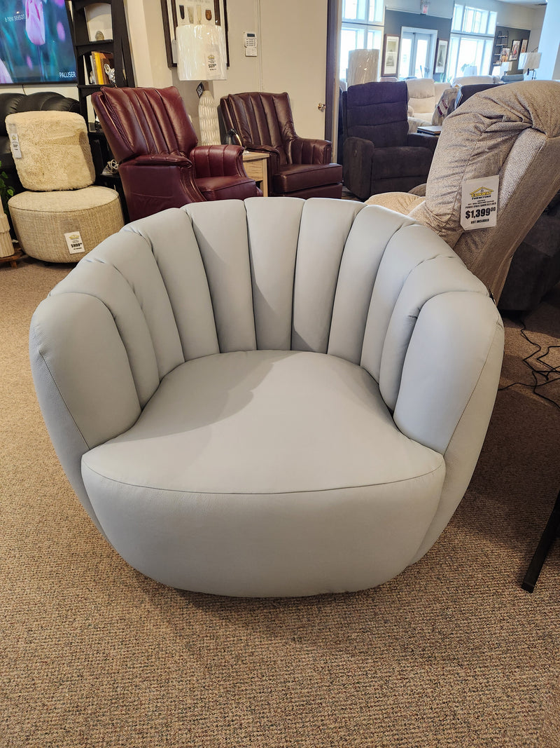 The Palliser 77109-G3 Jules Swivel Glider, light gray with a rounded barrel back, is shown in a furniture showroom.