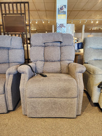 The Golden Aurora PL480 Power Lift Chair in gray with padded backrest and armrests is shown in a furniture showroom.