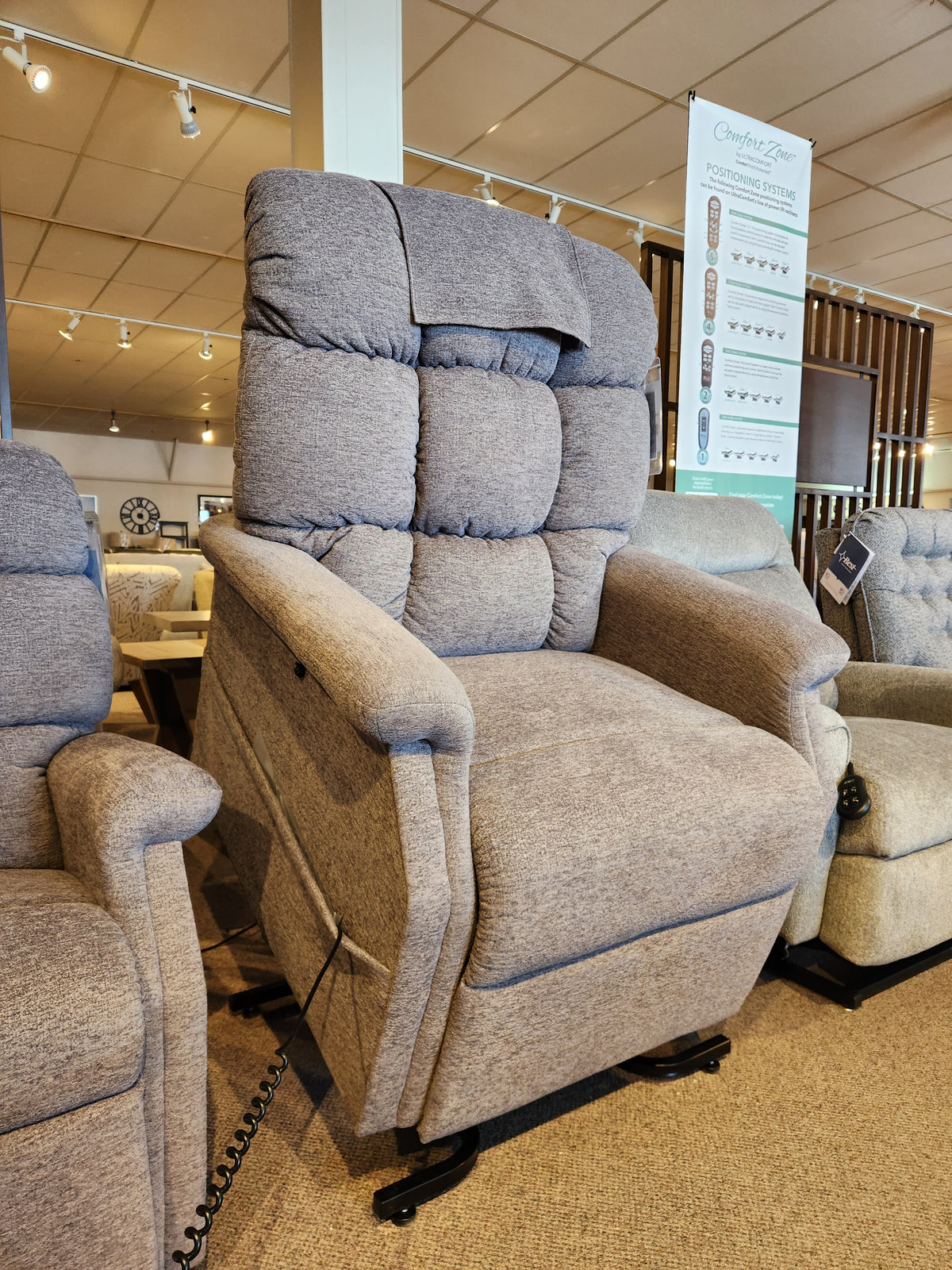 Golden Aurora PL480 Power Lift Chair in gray upholstery on showroom display with other chairs in the background.