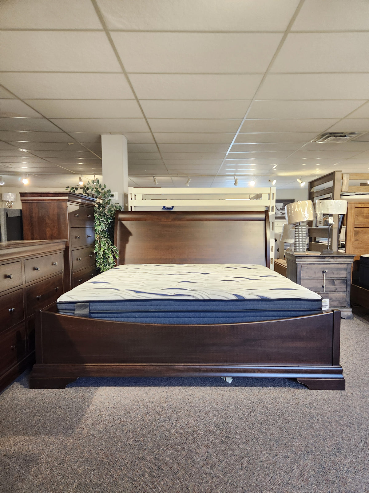 The Vokes 260 King Rustique Sleigh Bed in wormy maple is on display with dressers and nightstands in a showroom.