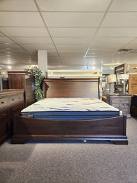 The Vokes 260 King Rustique Sleigh Bed in wormy maple is on display with dressers and nightstands in a showroom.