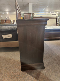 The Vokes 260 Louis Rustique 6 Drawer Dresser, a dark wood piece, is on display with beds and mattresses in-store.