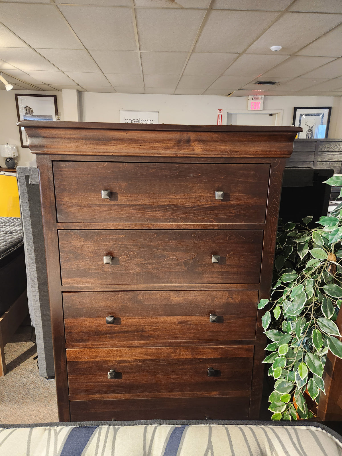 The Vokes 260 Louis Rustique chest features five drawers and square handles, shown near an artificial plant in the showroom.