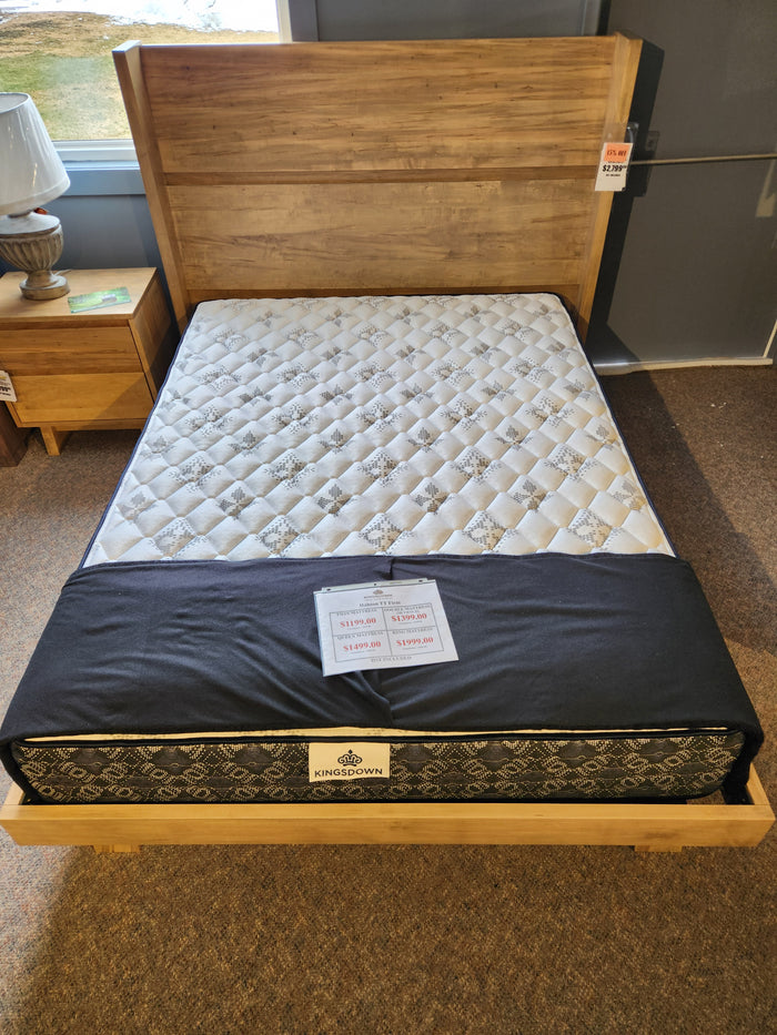 A wooden bed frame displays a KingsDown Halston TT Firm Mattress, with sale signs on the mattress.