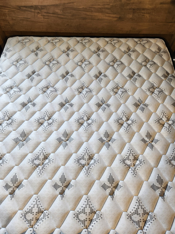 A close-up of the KingsDown Halston TT Firm Mattress with a wooden headboard in the background.