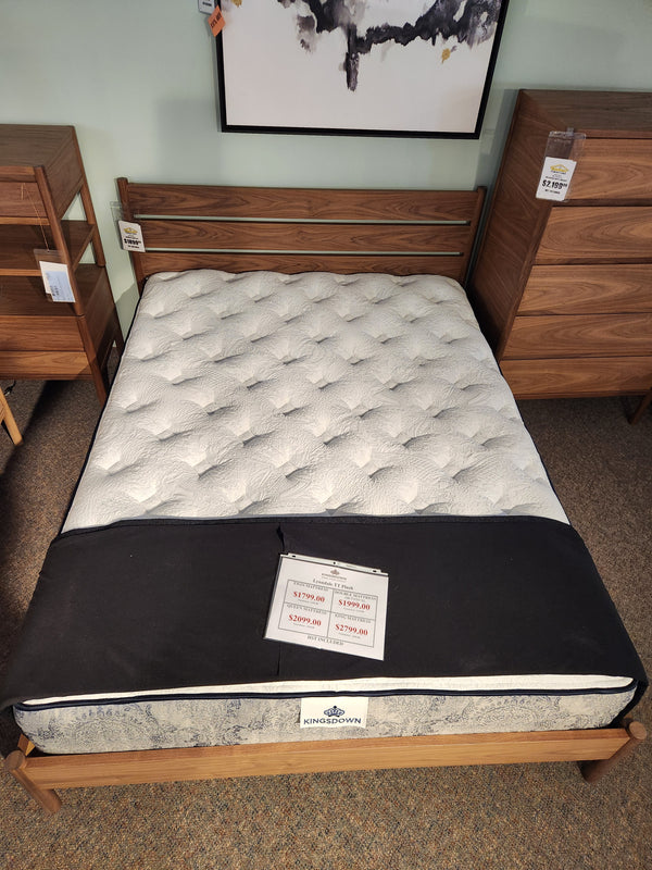 A KingsDown Lynndale TT Plush Mattress rests on a wooden bed frame between two dressers with price tags.